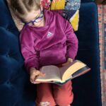 View from above of child reading a book on a blue couch.