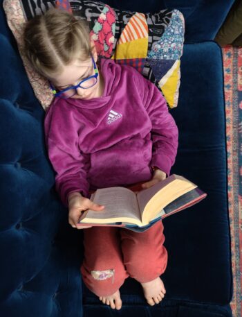 View from above of child reading a book on a blue couch.