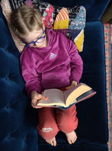 View from above of child reading a book on a blue couch.