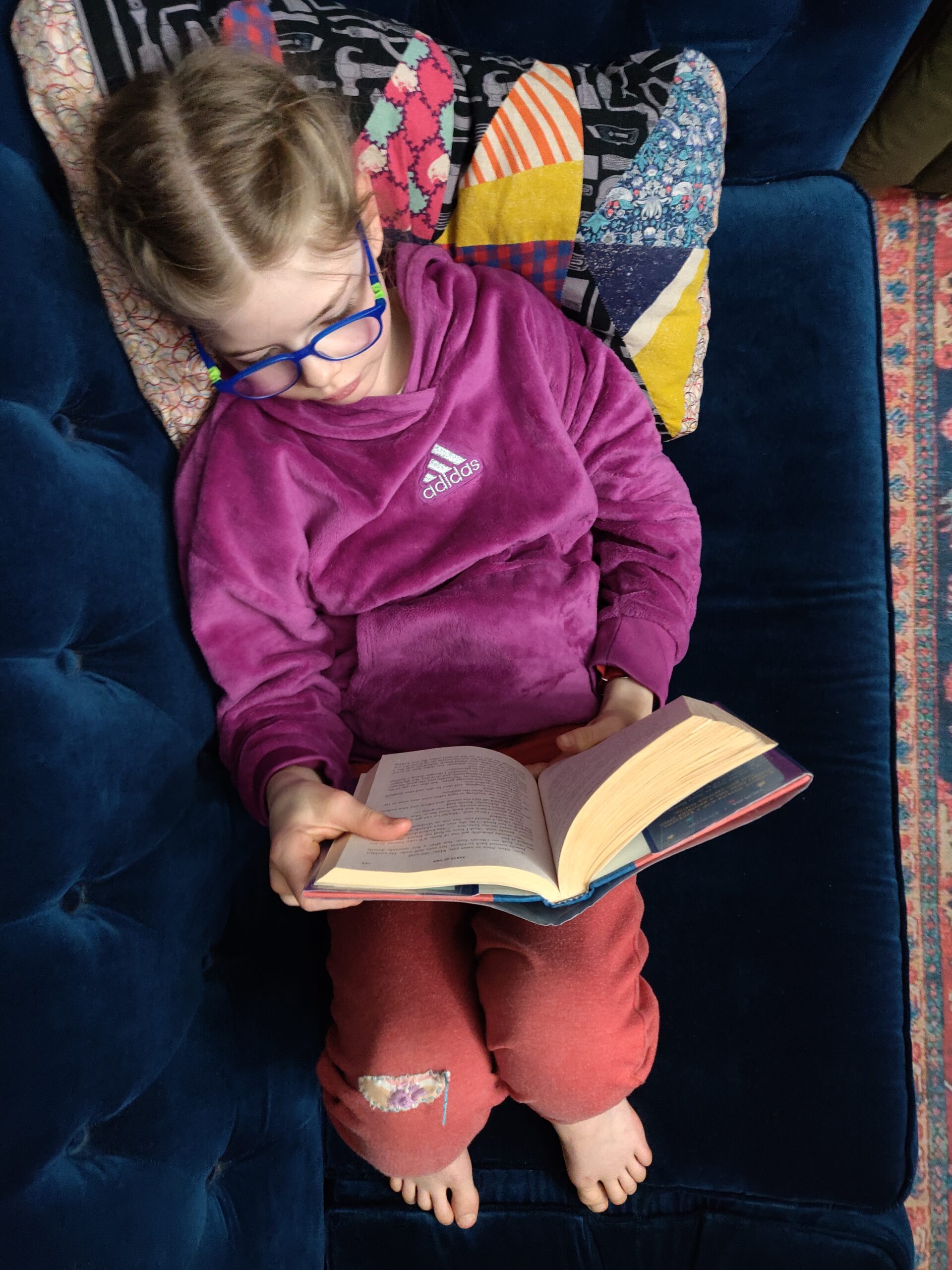 View from above of child reading a book on a blue couch.